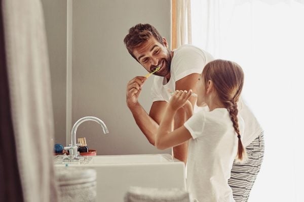 Vater und Tochter im Bad beim Zähneputzen.