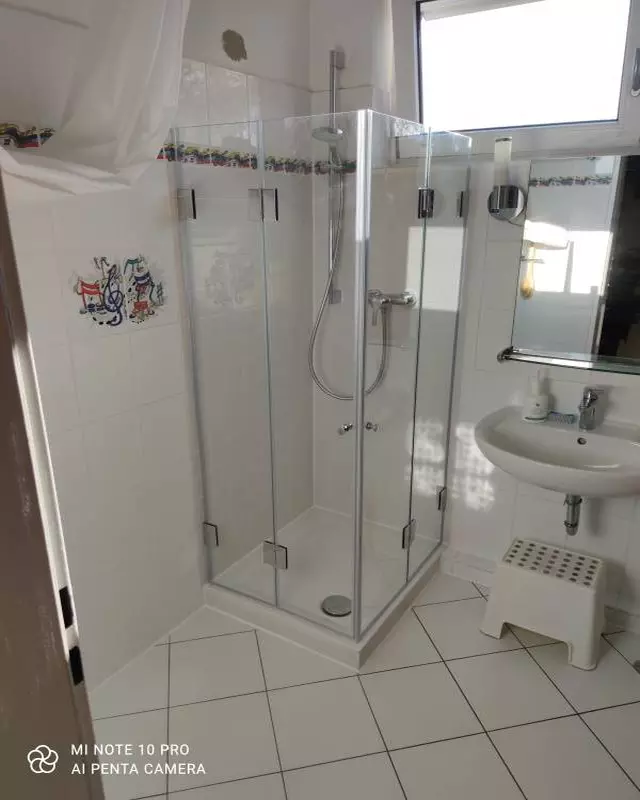 Dusche mit Falttüren F1W aus Glas auf Duschwanne in weiß gefliestem Badezimmer mit Fliesendekor