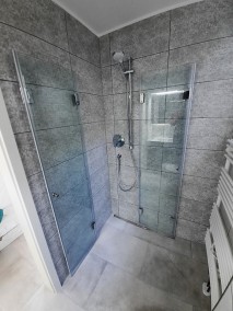 Eckdusche mit Falttüren F1W aus Glas in Badezimmer mit grauer Rückwand und Boden