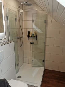 Eckduschkabine aus Glas mit Falttüren F1W auf Duschwanne in Bad mit weißen Wandfliesen und Dachschräge
