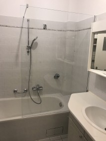 Duschwand PMPO aus Glas auf Badewanne  in grau verfliestem Badezimmer