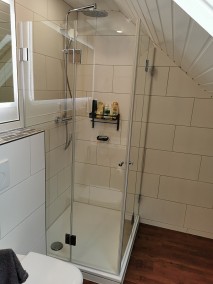 Falttür Eckdusche F1W auf Duschwanne in Badezimmer mit braunem Holzboden